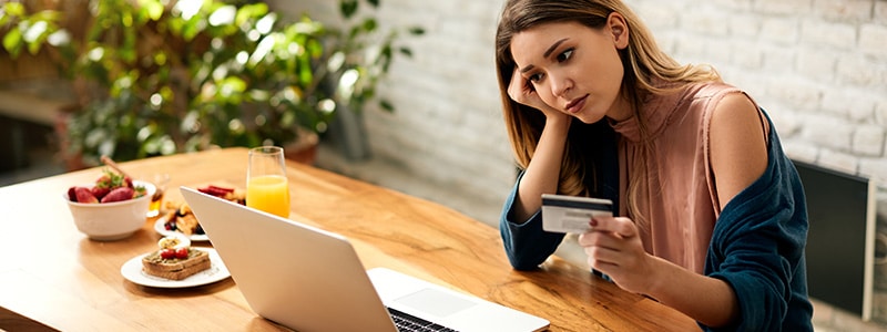 Mujer preocupada frente a computadora con tarjeta de credito en la mano.